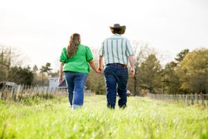 A couple walks through a green field on a sunny day.