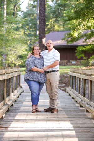 A couple poses together on a wooden bridge surrounded by lush forest.