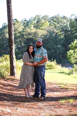 Couple posing for photos on pine needle covered ground in a forest setting.