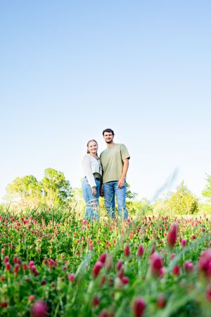 People standing together in a vibrant field of crimson clover under blue sky.