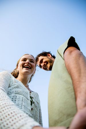 Low angle shot of couple against bright blue sky during outdoor photoshoot.