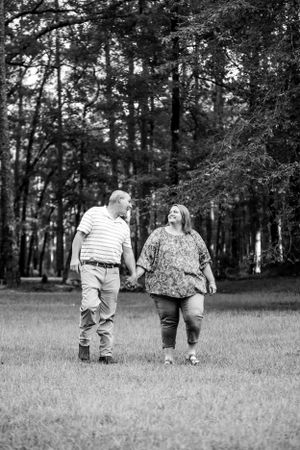 A black and white photo of a couple walking together in a wooded area.