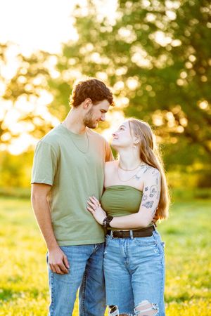 Couple in casual attire embracing in a sunlit meadow during sunset.