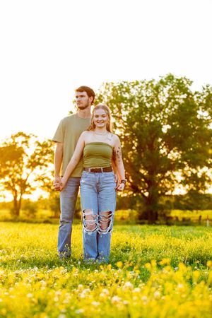Couple walking through a field of yellow wildflowers during golden hour.