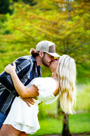 A romantic couple shares a passionate dip kiss in a sunlit garden setting.