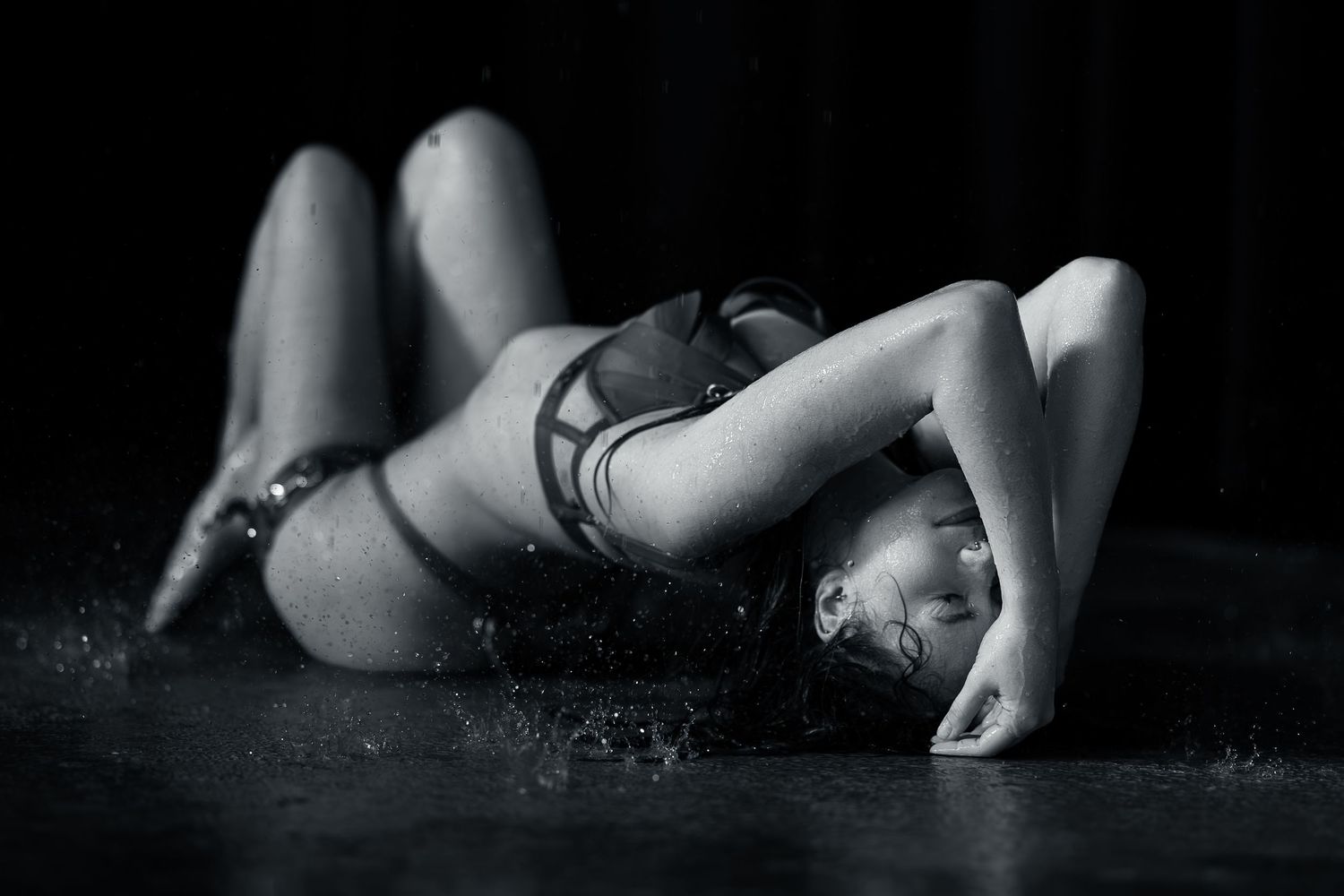Black and white photo of a woman in lingerie lying on a wet floor in an artistic dance pose.