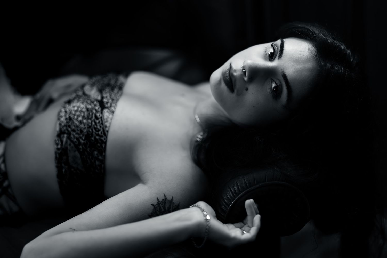 Black and white boudoir photograph showing person in lace lingerie reclining against dark background.