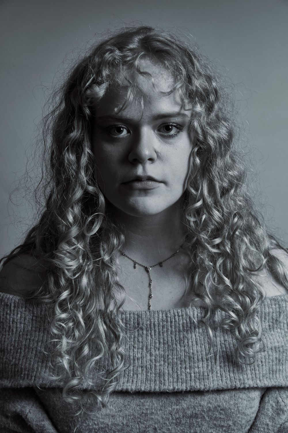 Black and white portrait of a woman in a studio, close up shot of a serious stare and she has curly hair.