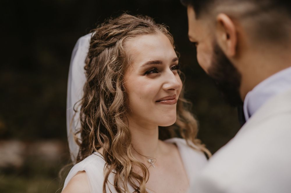Close up of bride with curly hair smiling at groom during outdoor wedding.