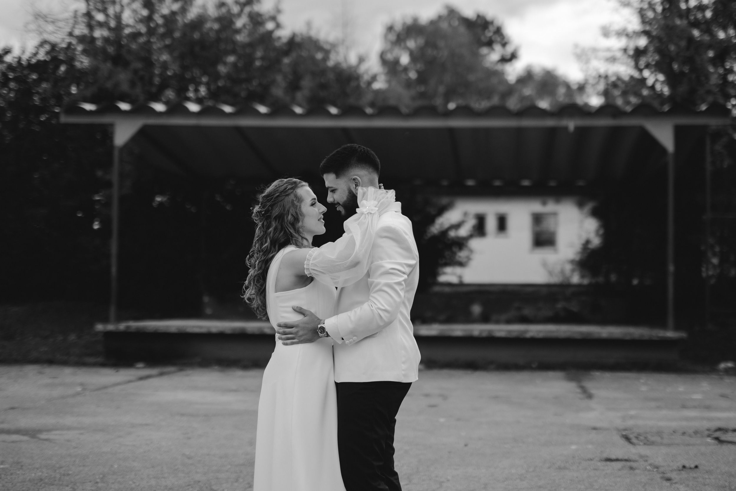 Black and white photo of newlyweds embracing during outdoor wedding ceremony.