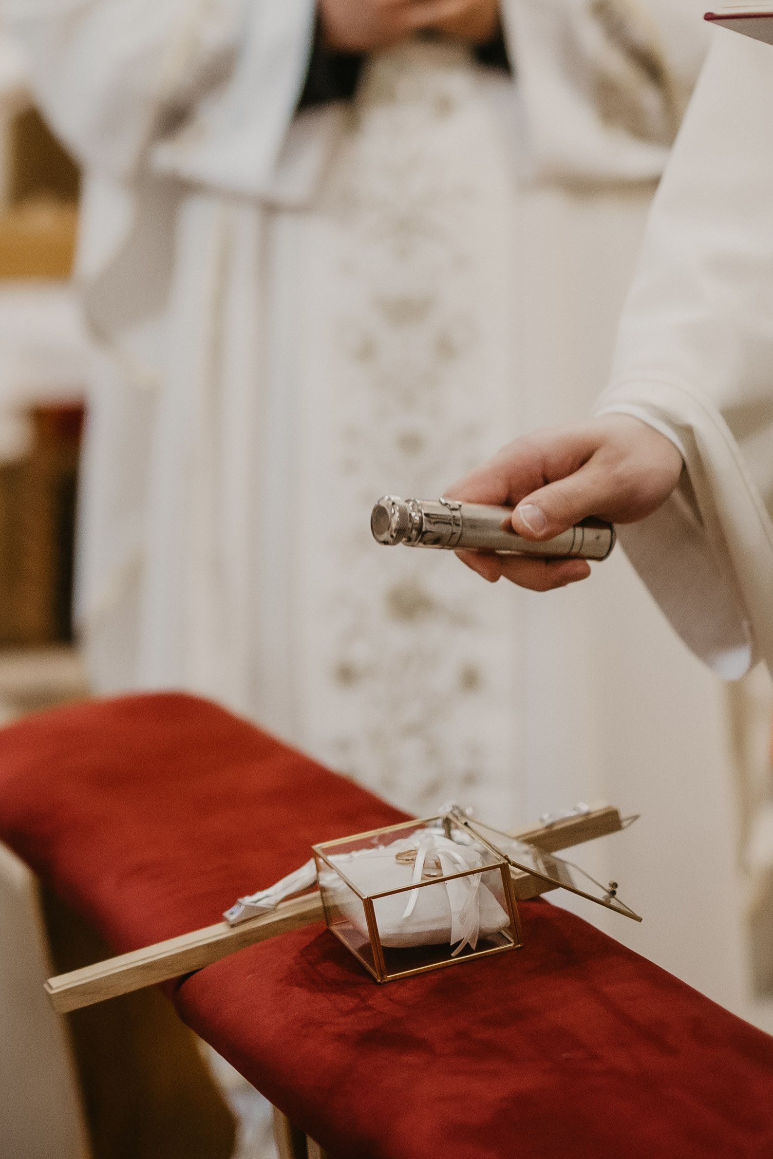 Close-up of ceremonial Catholic wedding items on red fabric during a church ceremony.