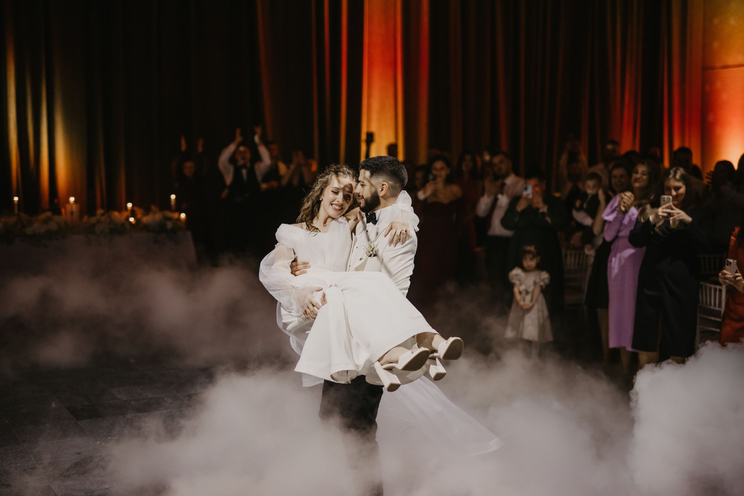 A couple performs a dramatic dance move amid smoke effects at their wedding celebration.