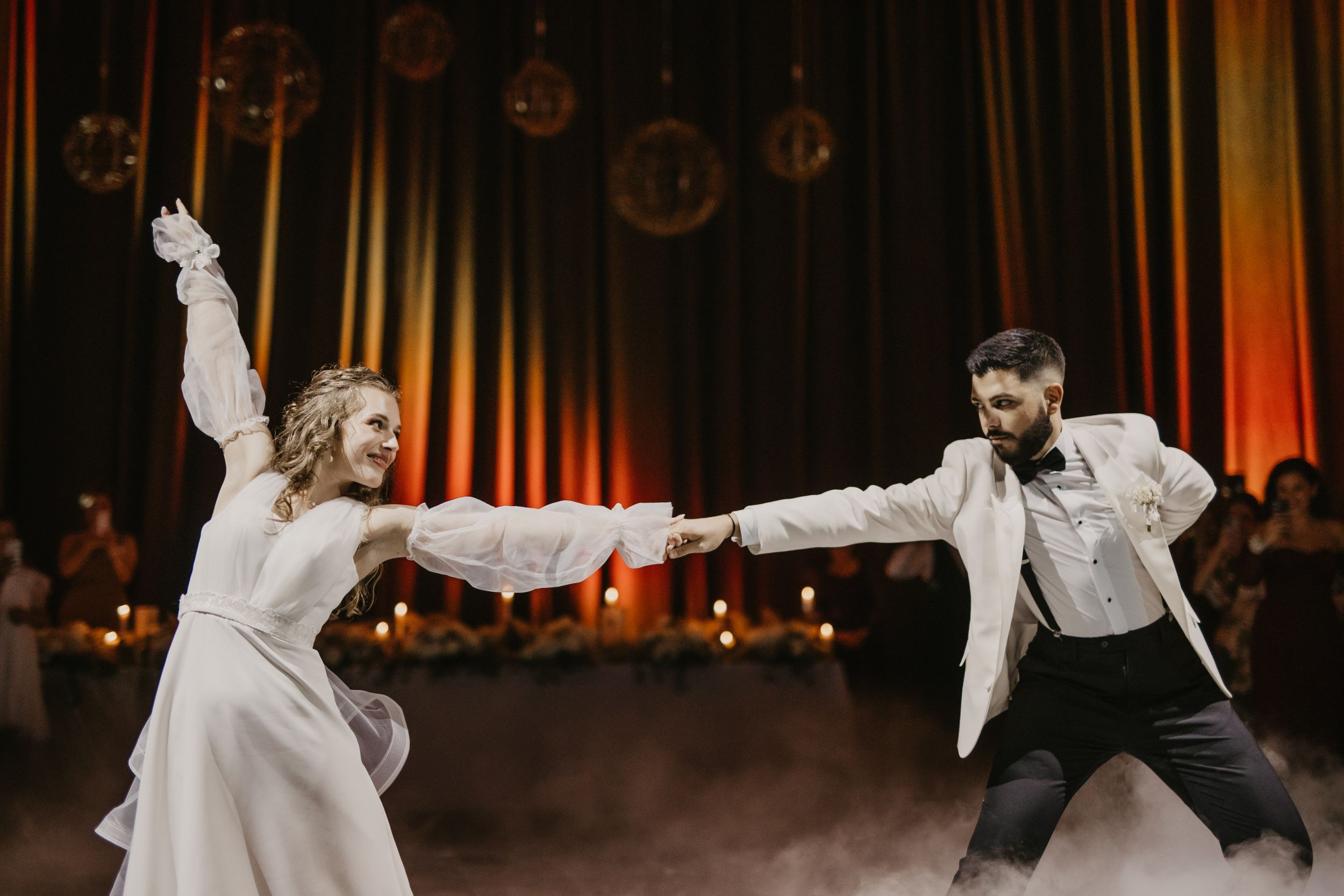 Couple performs energetic first dance at wedding reception with dramatic lighting and hanging decorations.