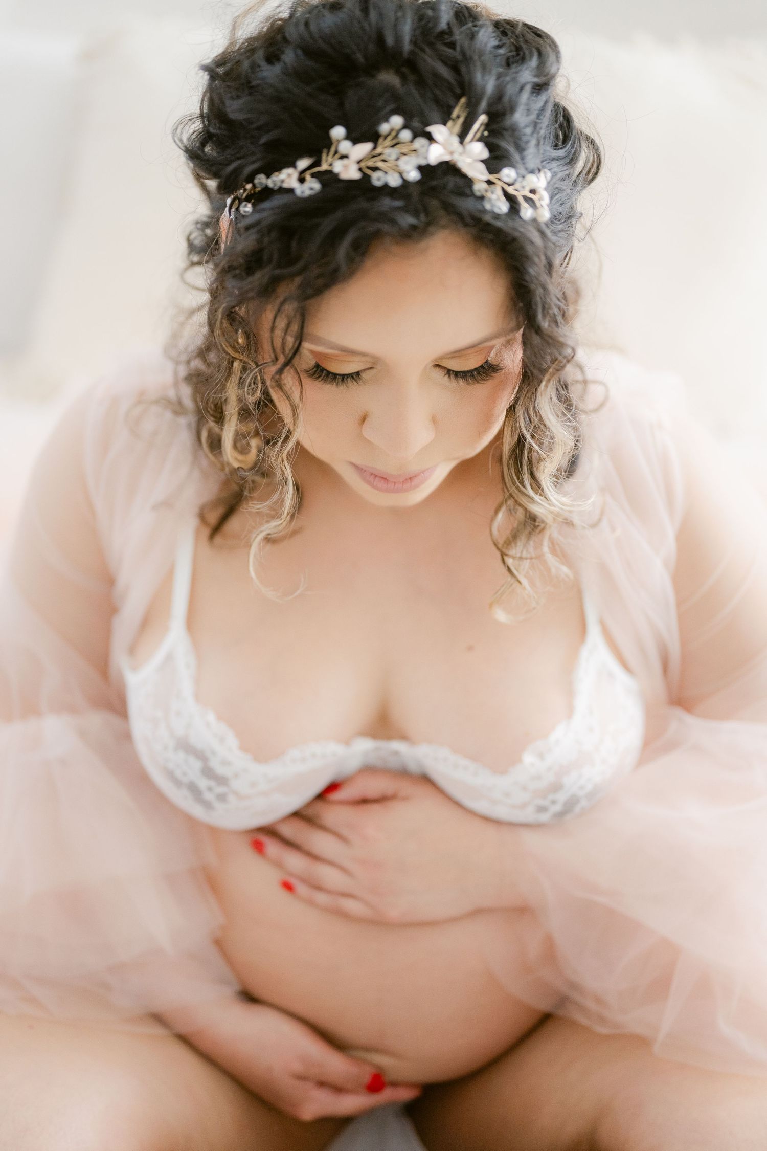 An intimate maternity portrait shows a floral headpiece and lace attire against a light background.