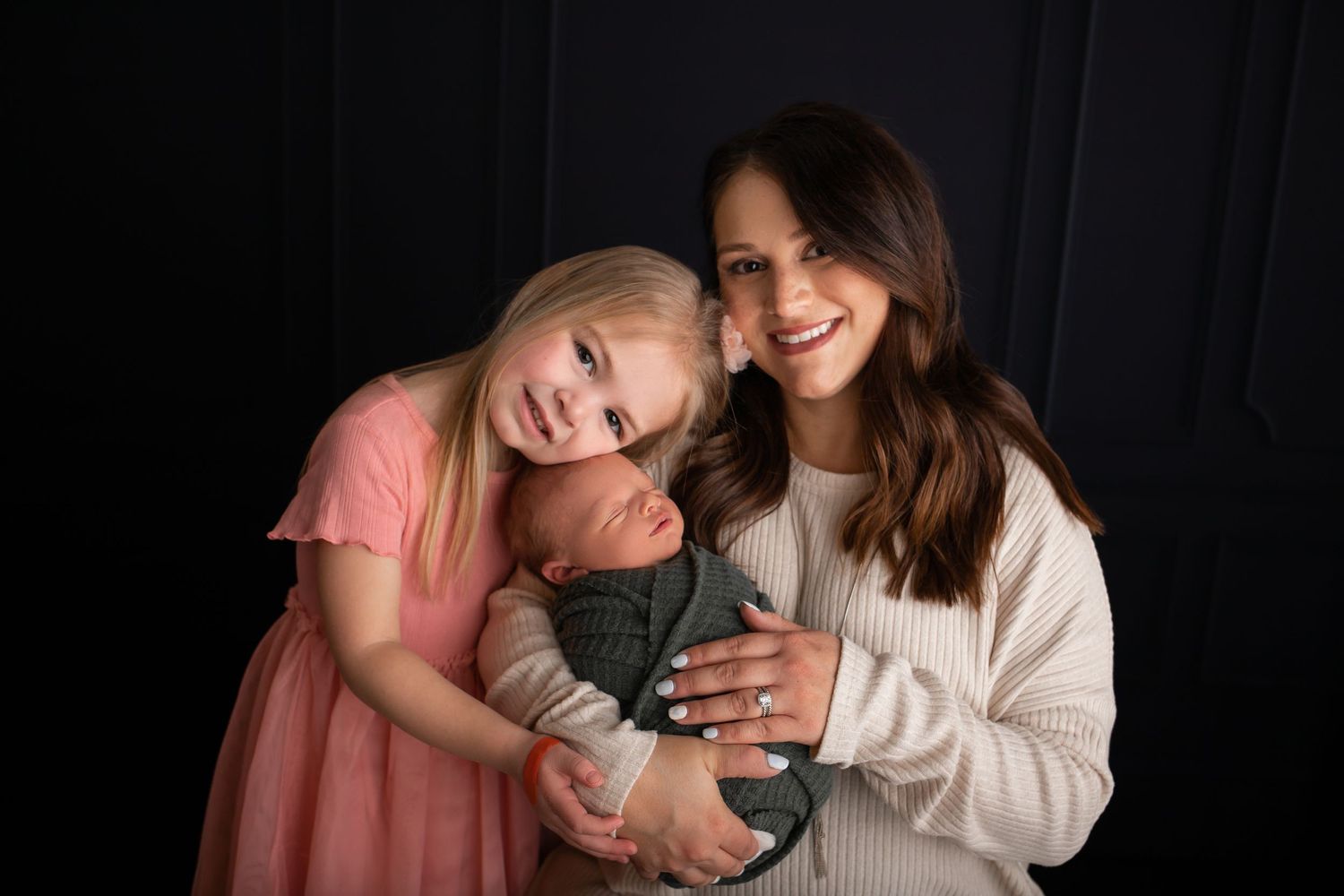 Studio portrait of family members embracing against dark backdrop.