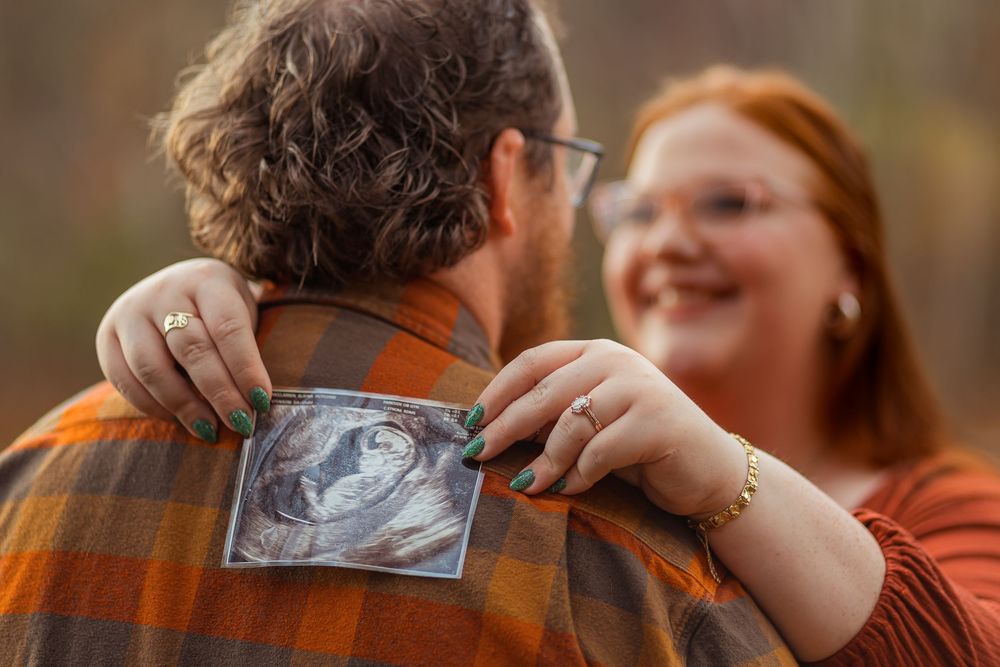 Happy couple shares an intimate moment while holding up an ultrasound photo during a pregnancy announcement.