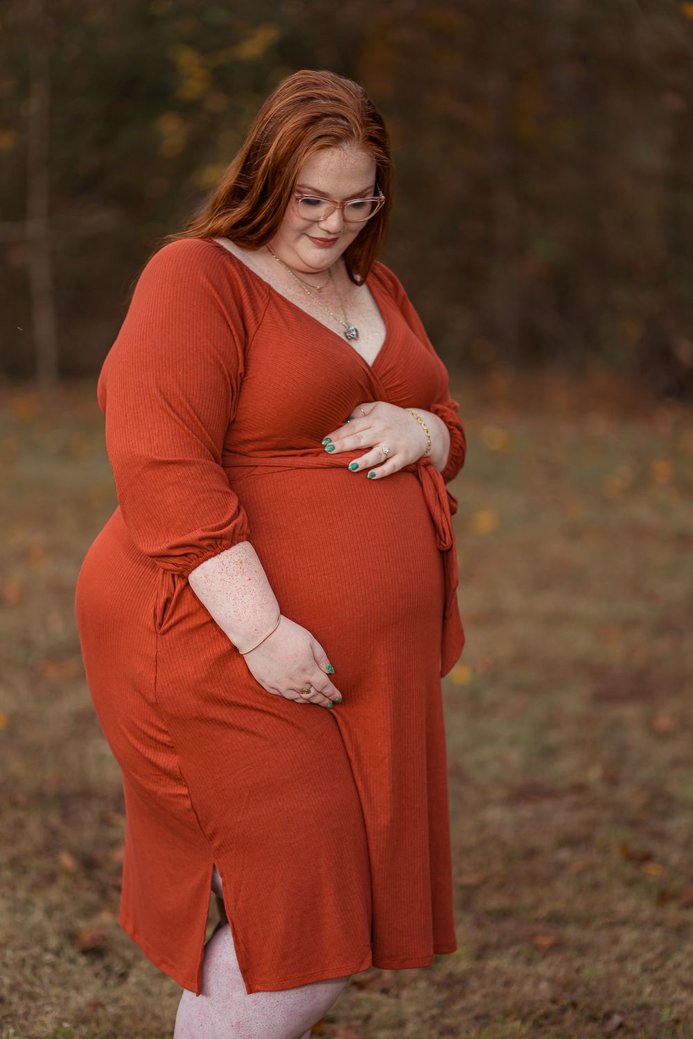 Pregnant woman in red sweater holds her baby bump while standing outdoors during autumn.
