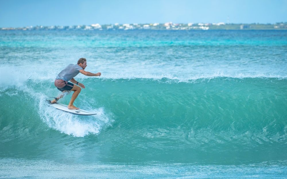 Surfer riding turquoise wave with perfect form during daytime at a tropical beach location.