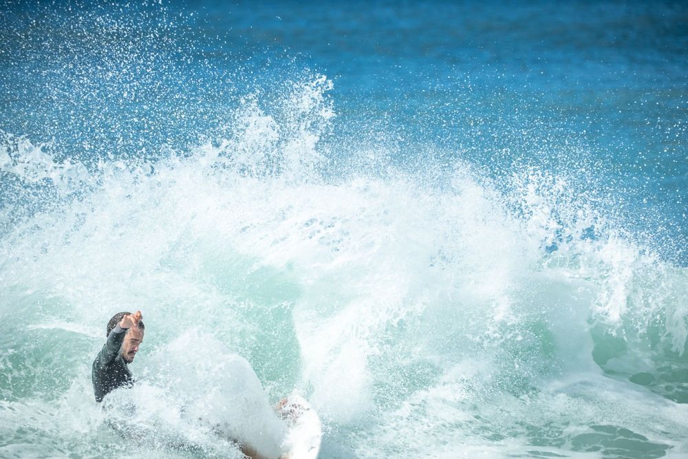 Powerful wave spray captures dramatic moment during surfing session in blue ocean waters.