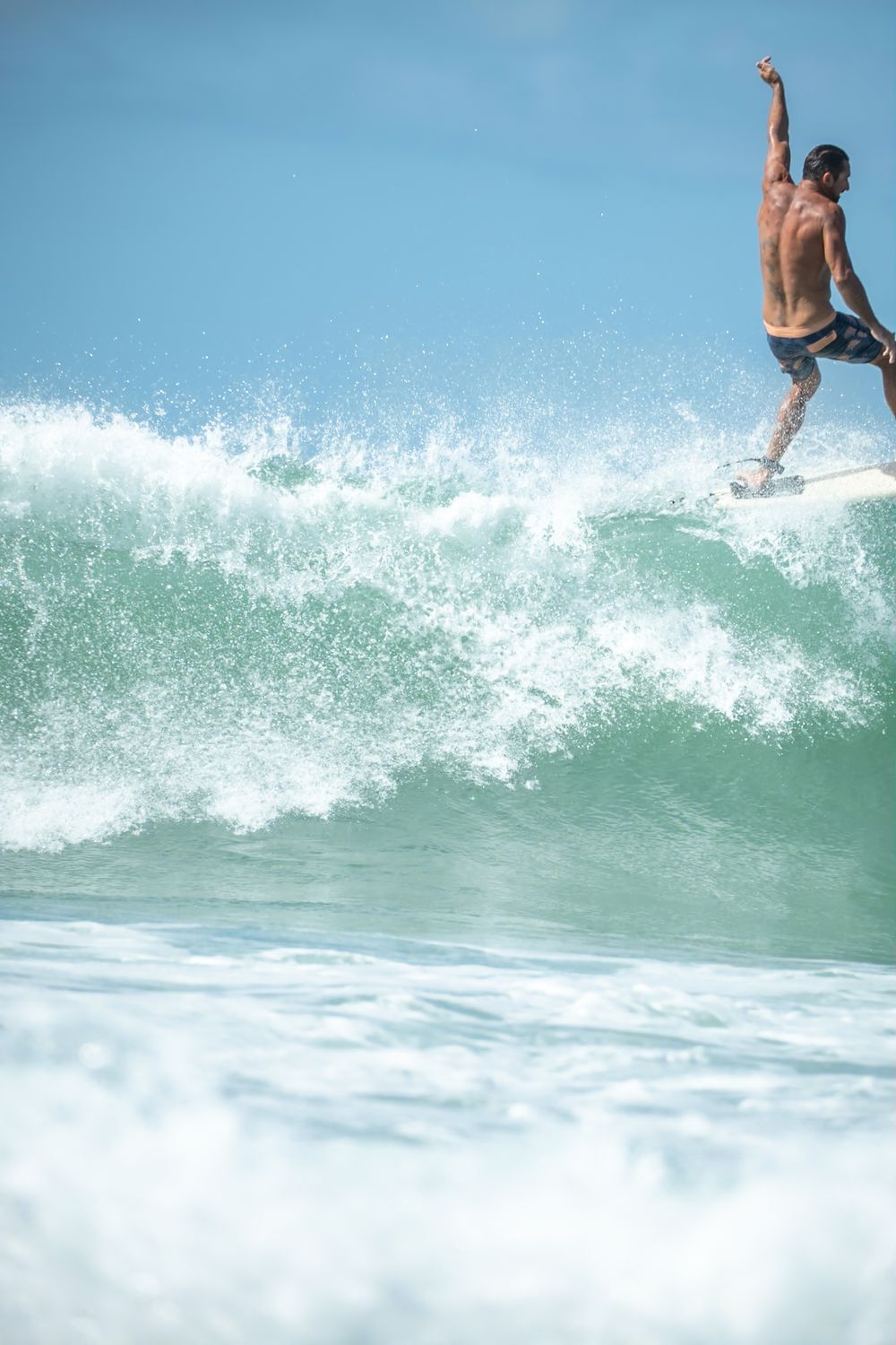 Surfer performing aerial maneuver at peak of crystal clear ocean wave against blue sky.