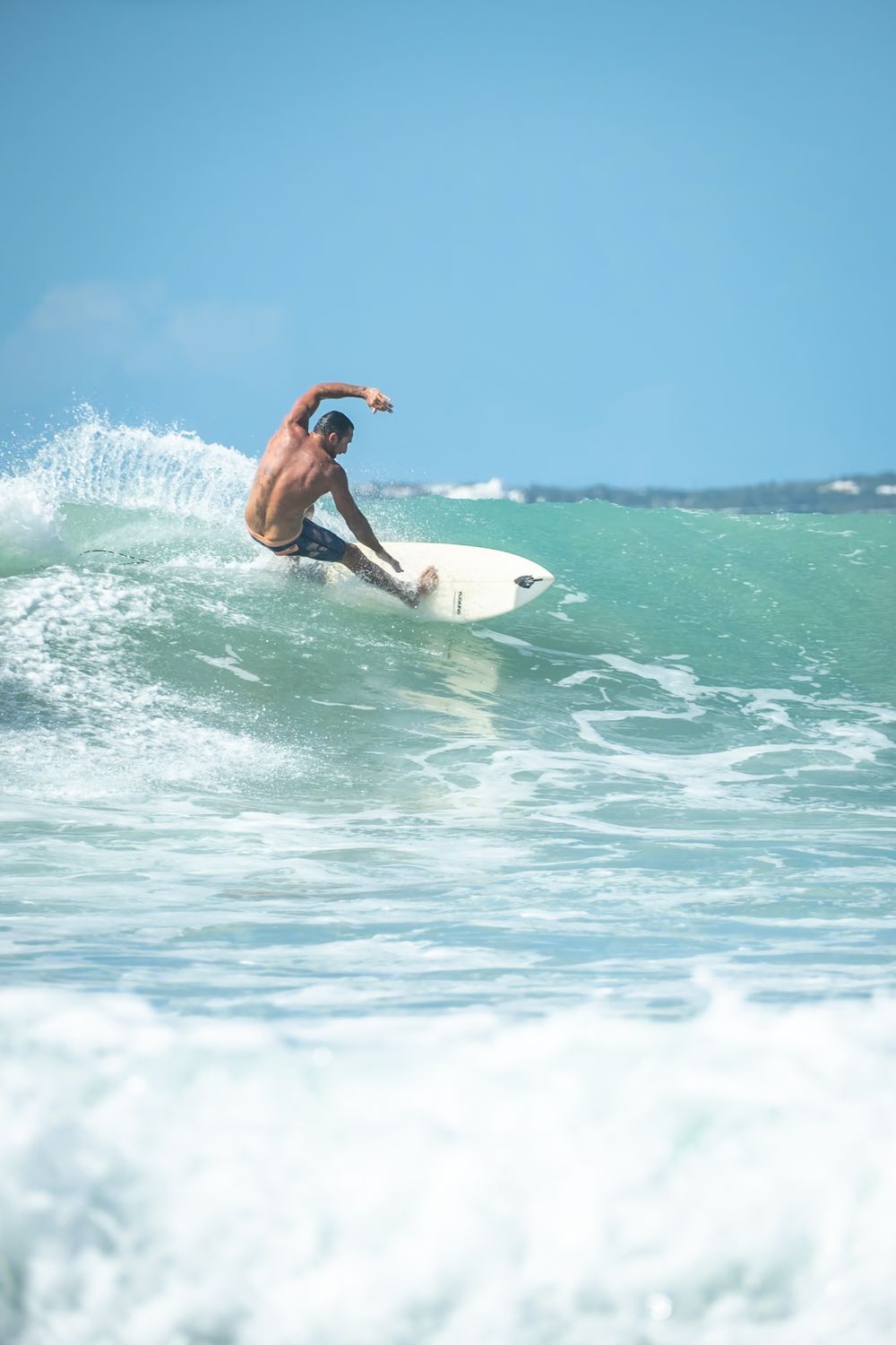 Graceful surfer carving through crystal clear wave during perfect beach conditions.