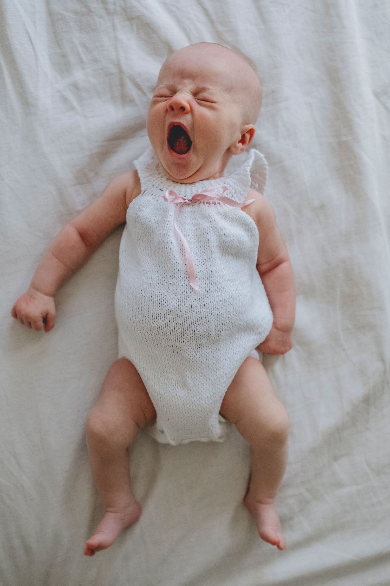 bebé recién nacido sobre la cama de sus padres bostezando