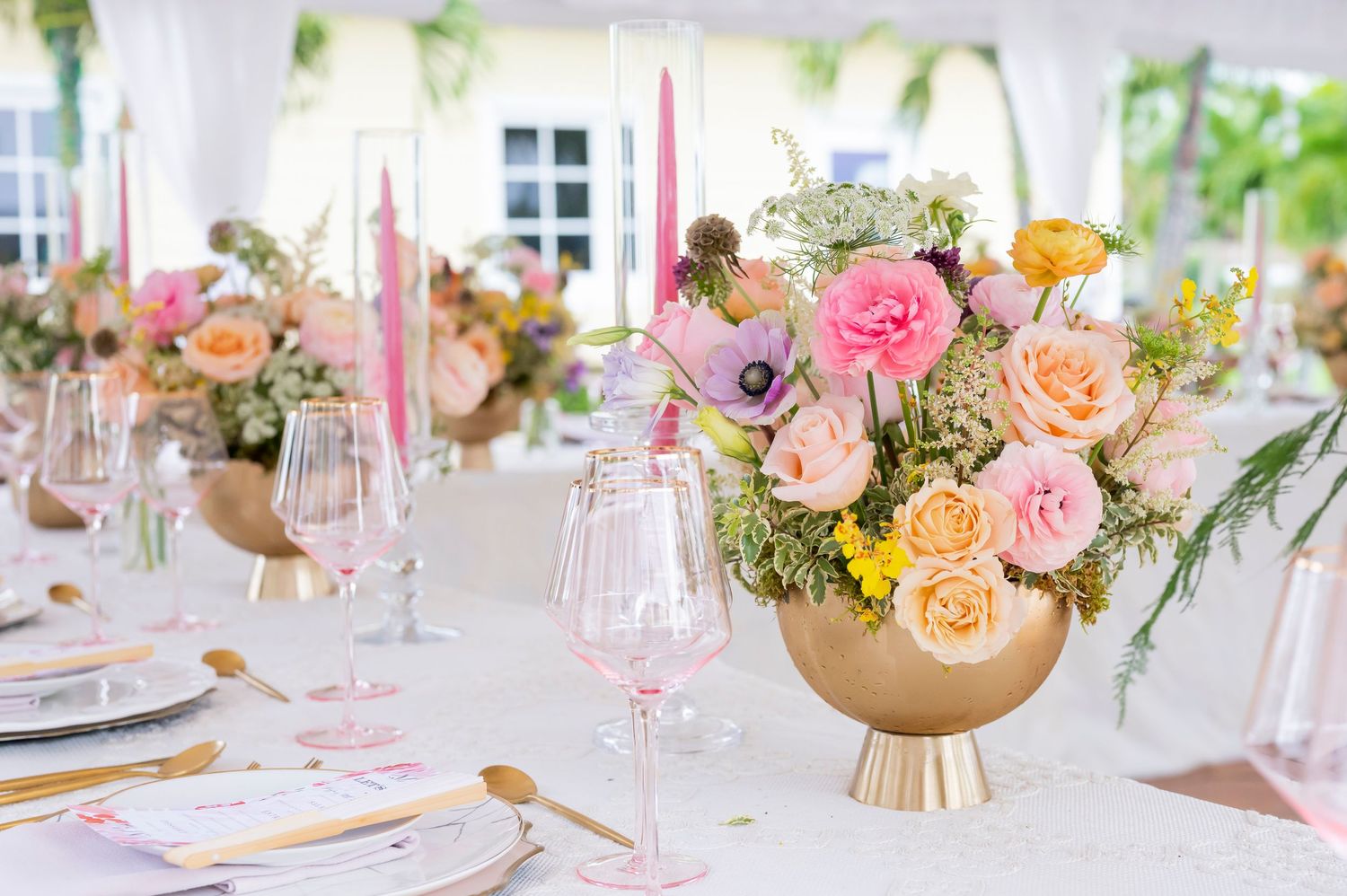 Elegant reception table setting with pink roses and delicate floral arrangements in gold vases alongside pink candles.