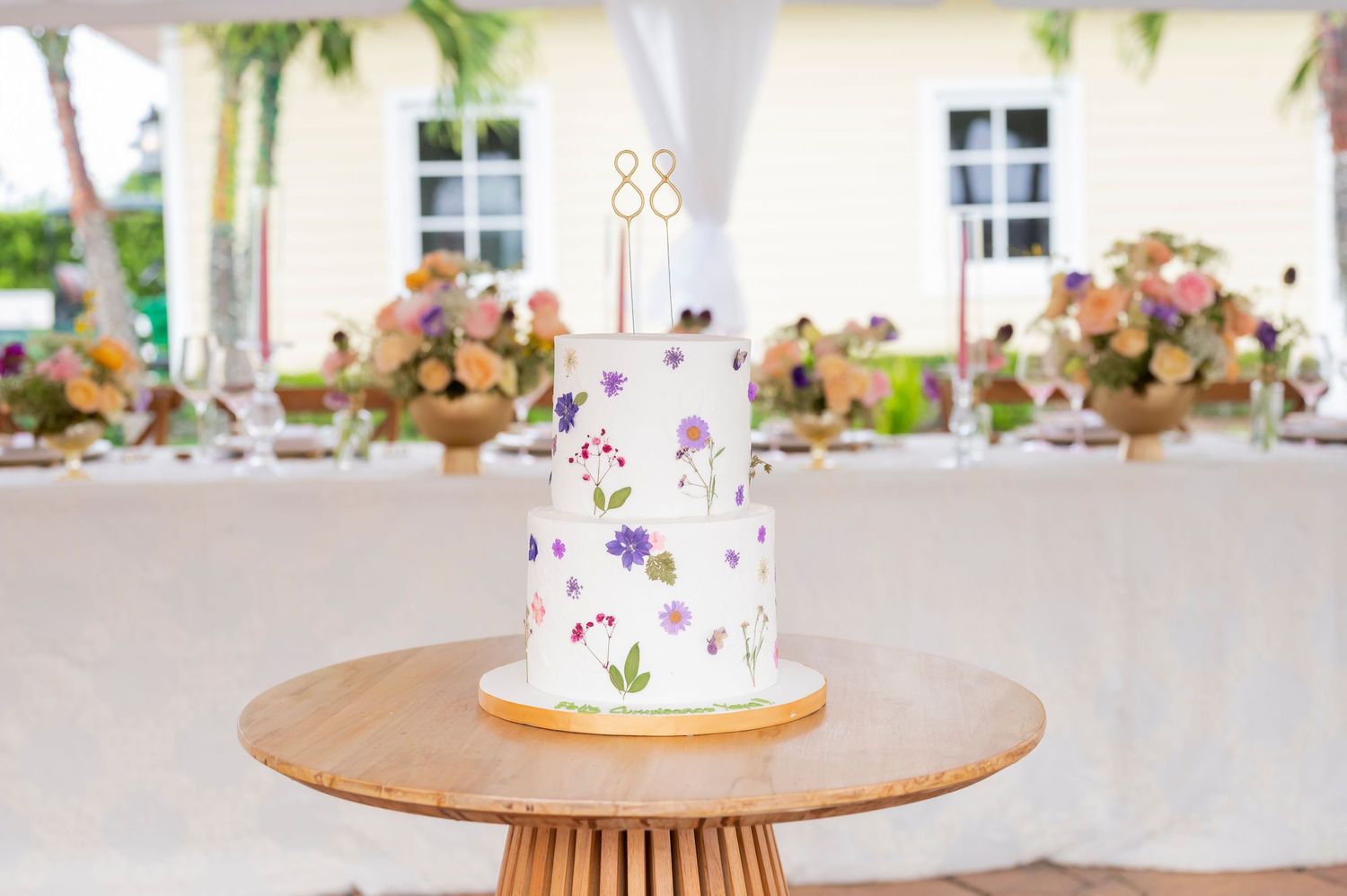 White cake decorated with purple and pink floral designs on a wooden pedestal table at an elegant reception venue.