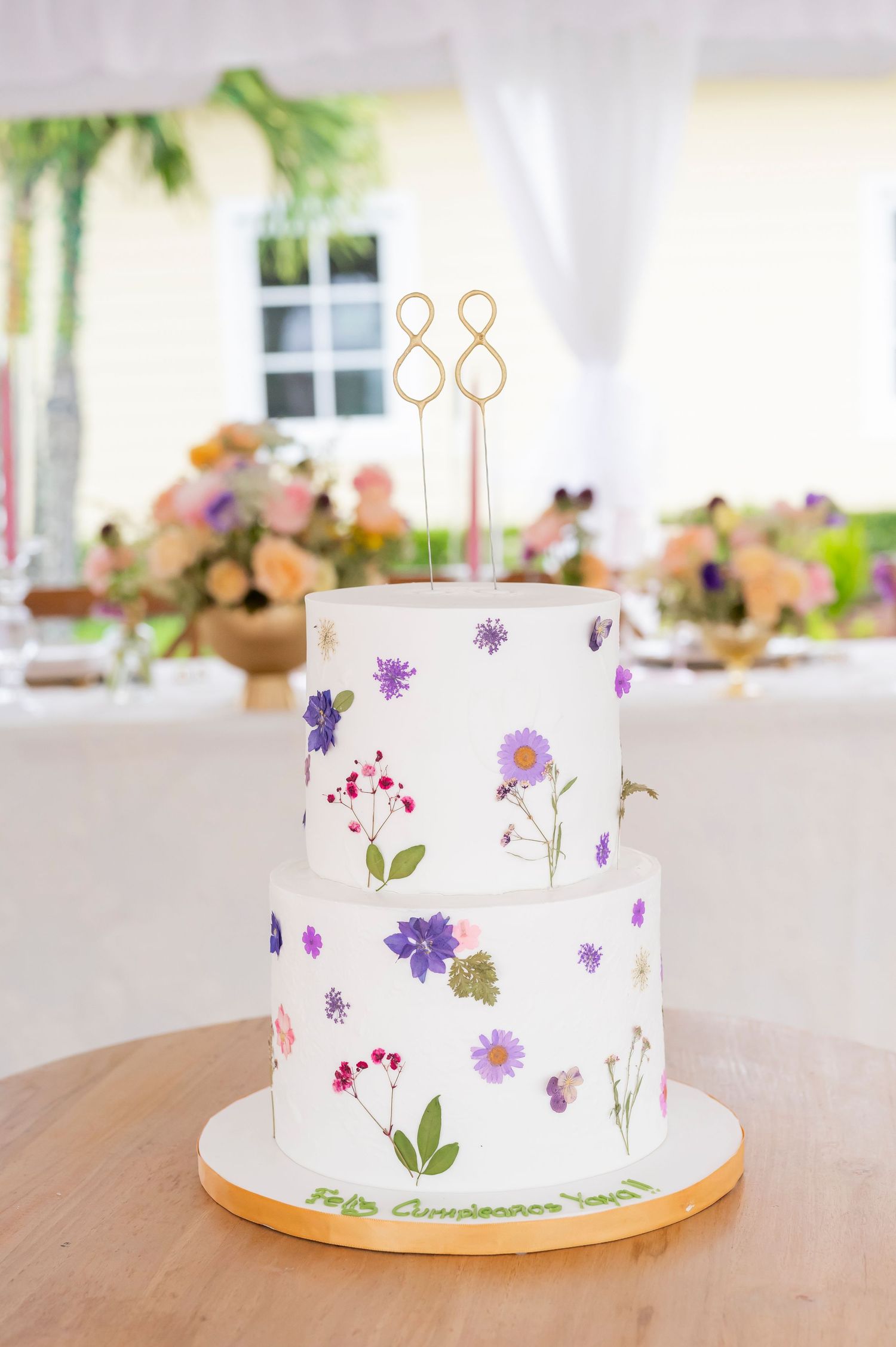 Two-tiered white cake decorated with delicate pressed wildflowers and topped with a gold number 88 cake topper.