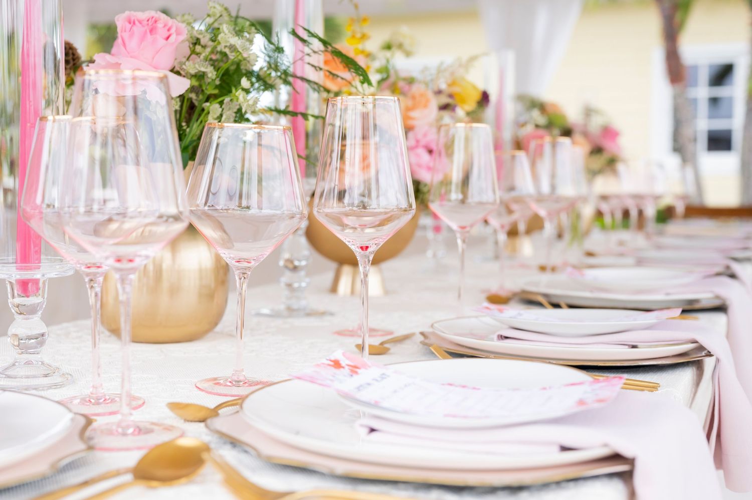 Elegant table setting with wine glasses, white plates, and pink floral centerpieces at a formal event.