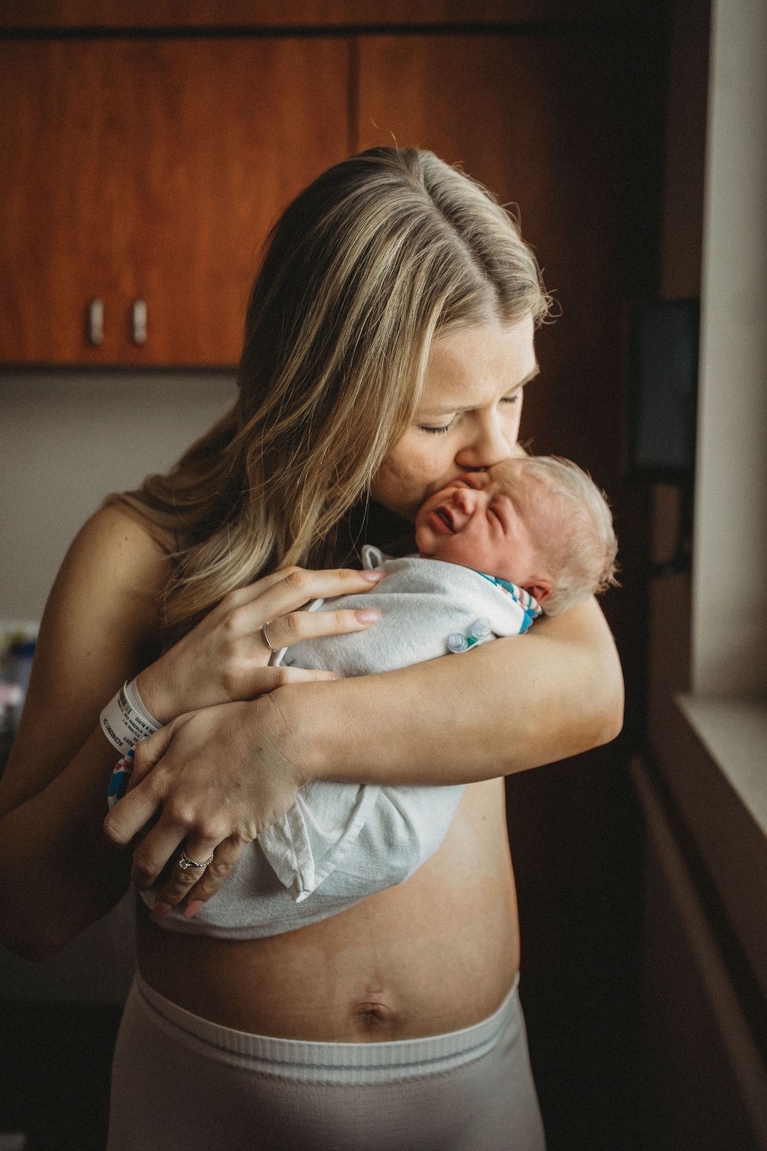 Intimate moment showing tender embrace in hospital room with wood cabinets.