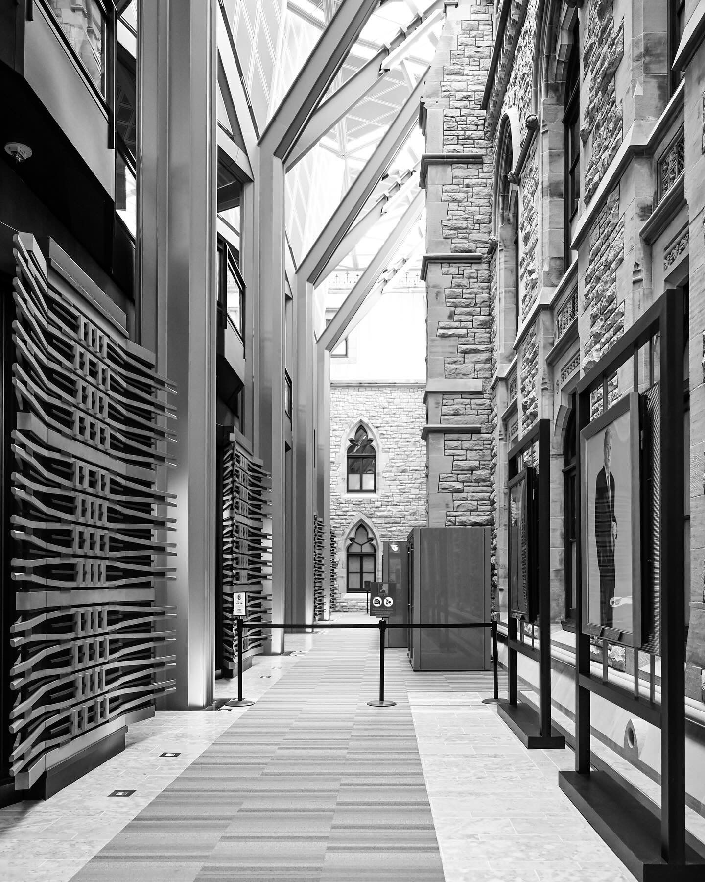 Stone corridor with modern architectural elements featuring glass panels and gothic archways.