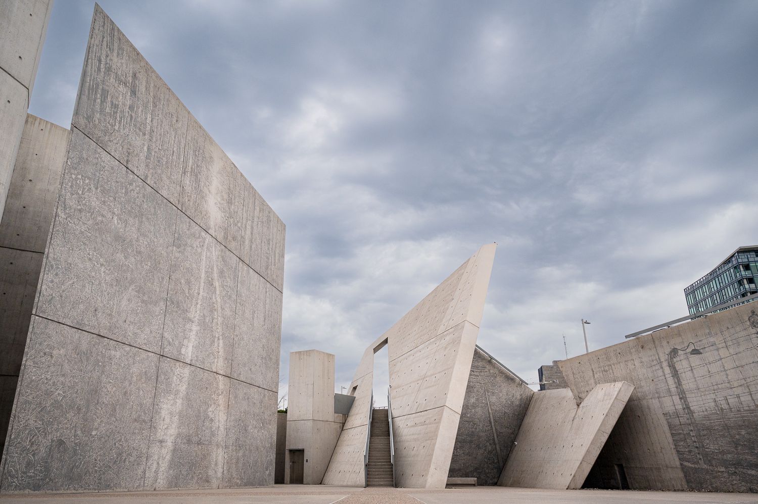 Modern concrete architectural structure with angular walls against cloudy sky.