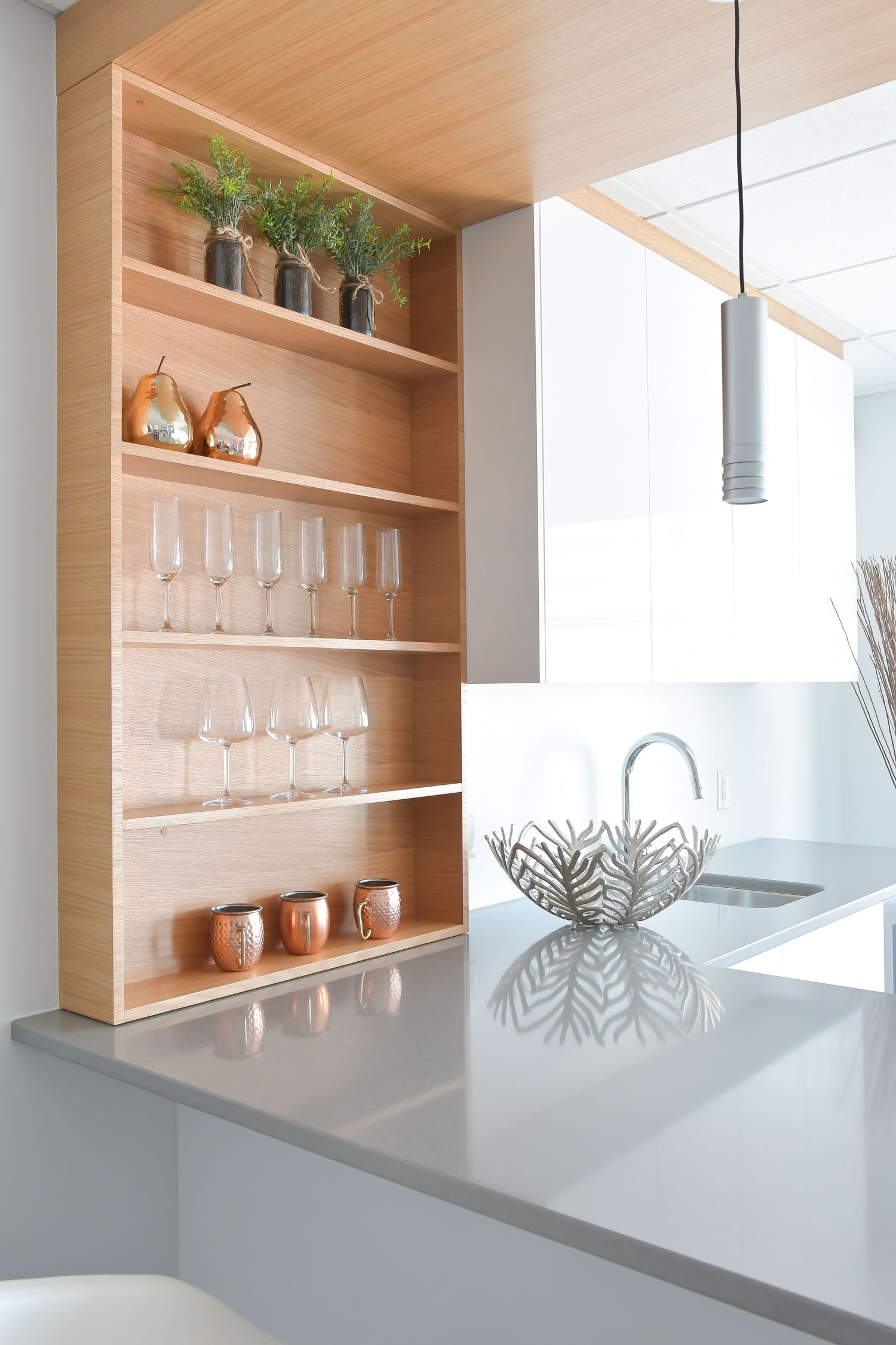 Contemporary built-in shelving unit displaying glassware and decorative items with warm wood finish.