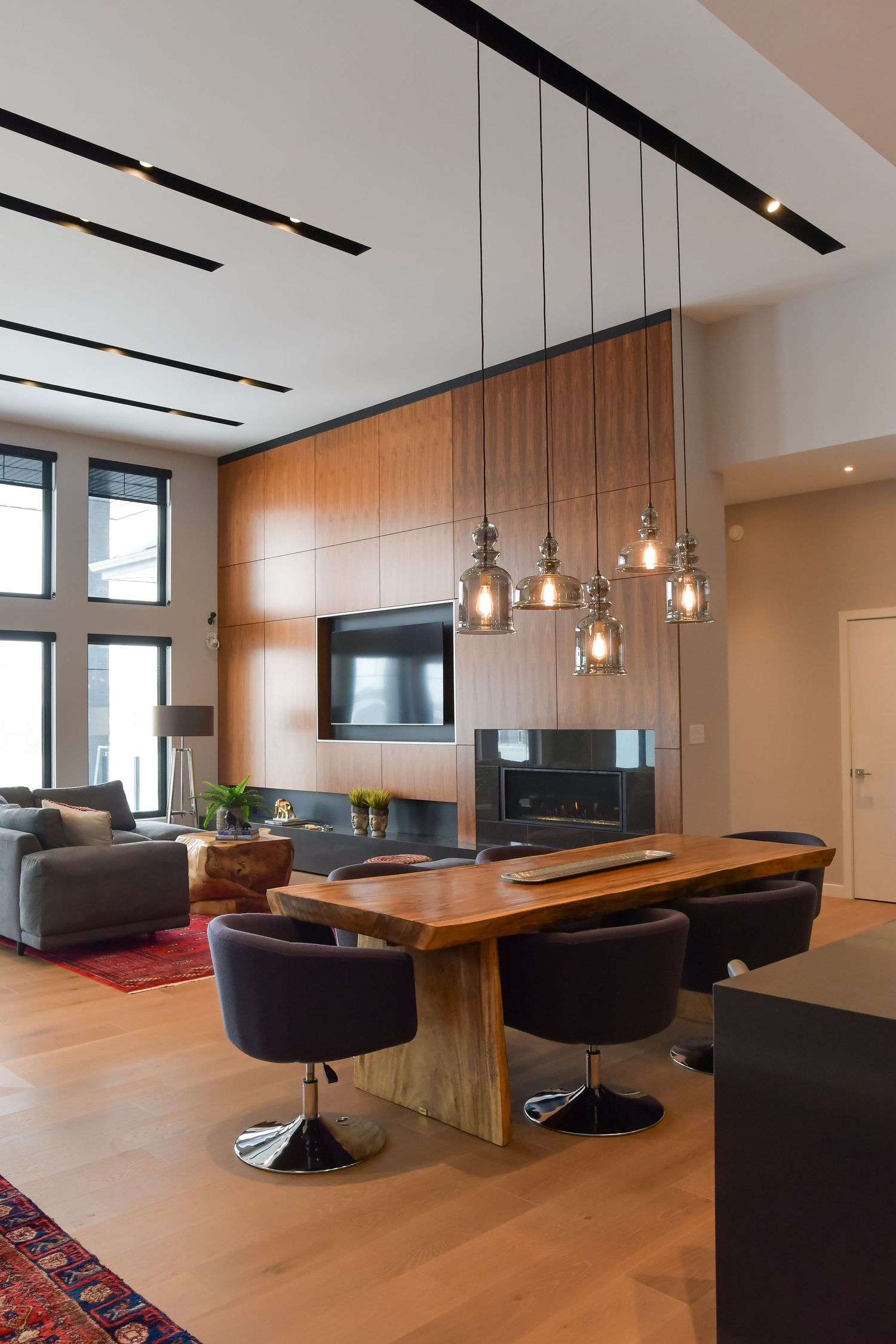 Modern living space with hanging pendant lights and wood dining table surrounded by purple chairs.