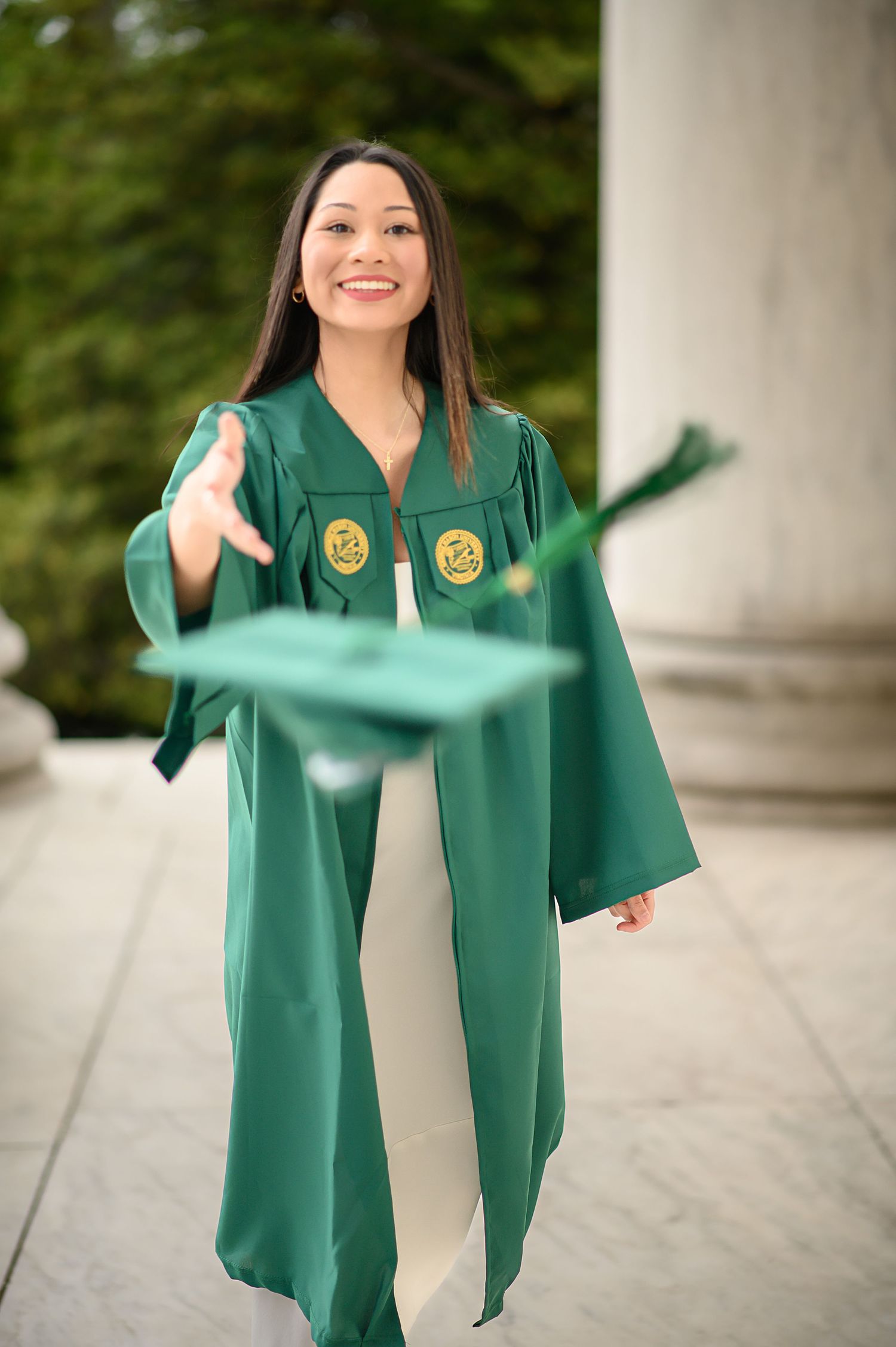Graduate in emerald green academic regalia celebrating on campus.