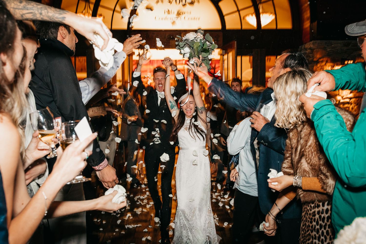 A bride and groom raise their hands in celebration during their grand exit. Guests throw flower petals in Seattle.
