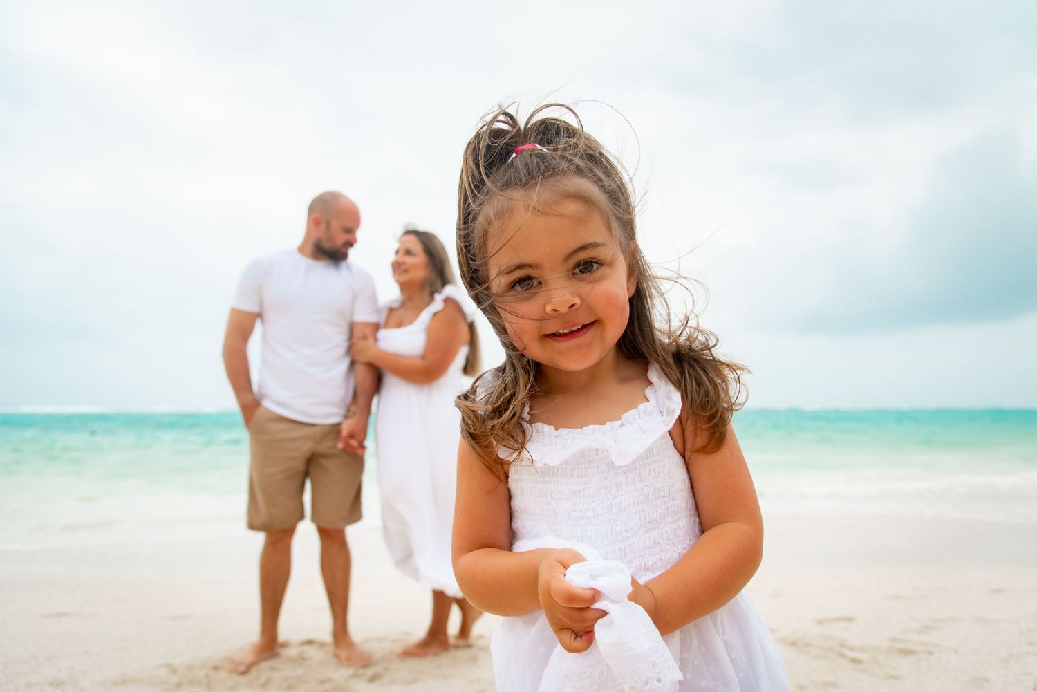 Mom and dad looking at each in the background while daughter looks at the camera up close