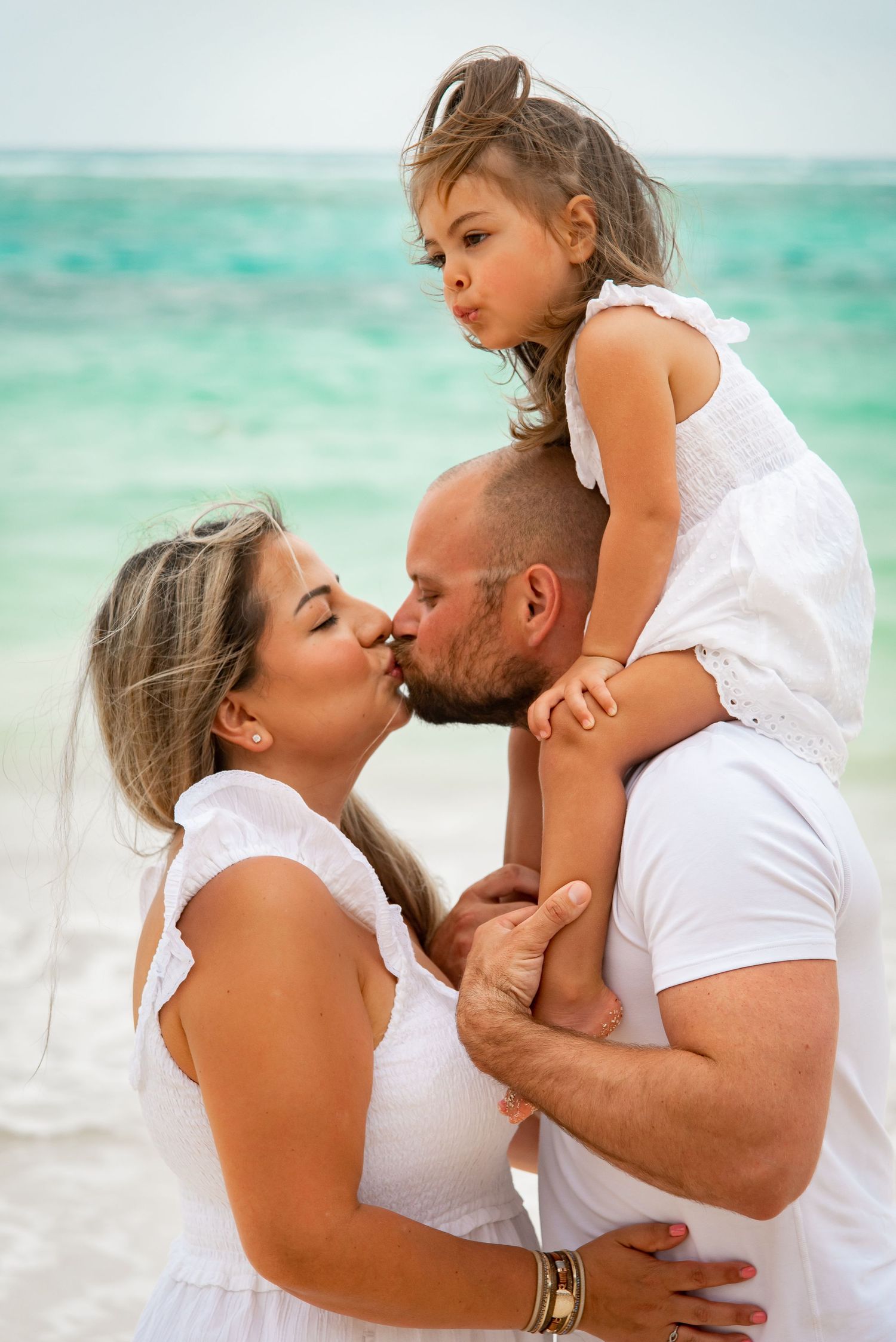 close up of mom and dad kissing wile carrying their daughter on dad's shoulder