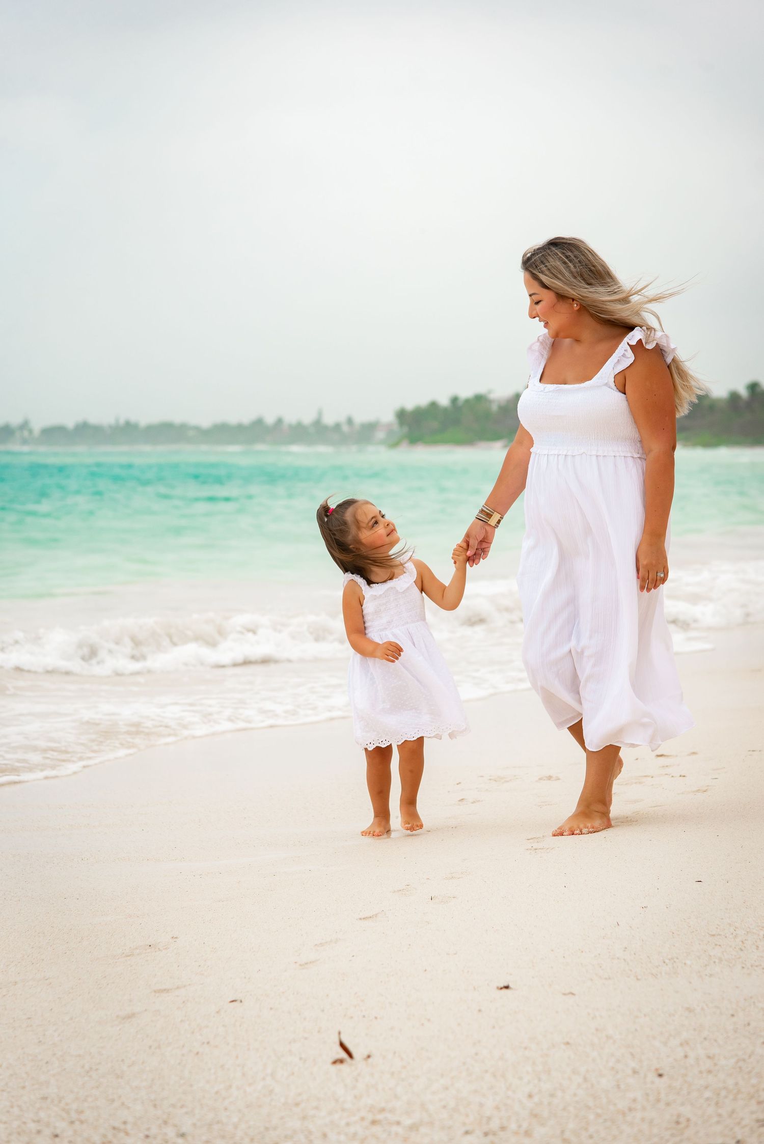 portrait of mom and daughter walking by the beach of Akumal, holding hands while looking at each other