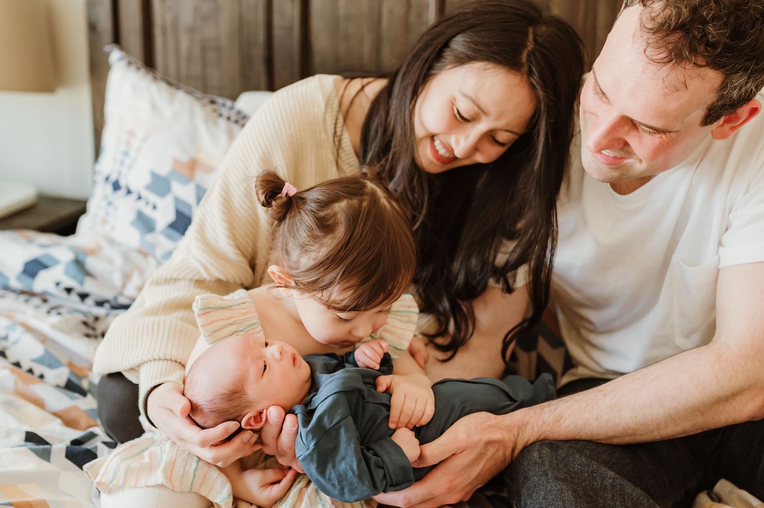 Parents tenderly care for their newborn baby in soft white bedding at home.