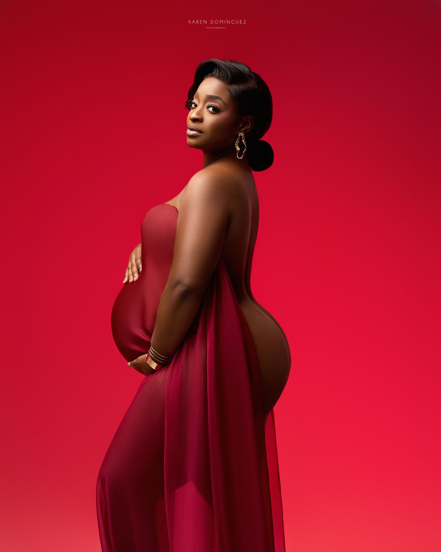 Elegant profile maternity photo of figure in black dress against gray background.