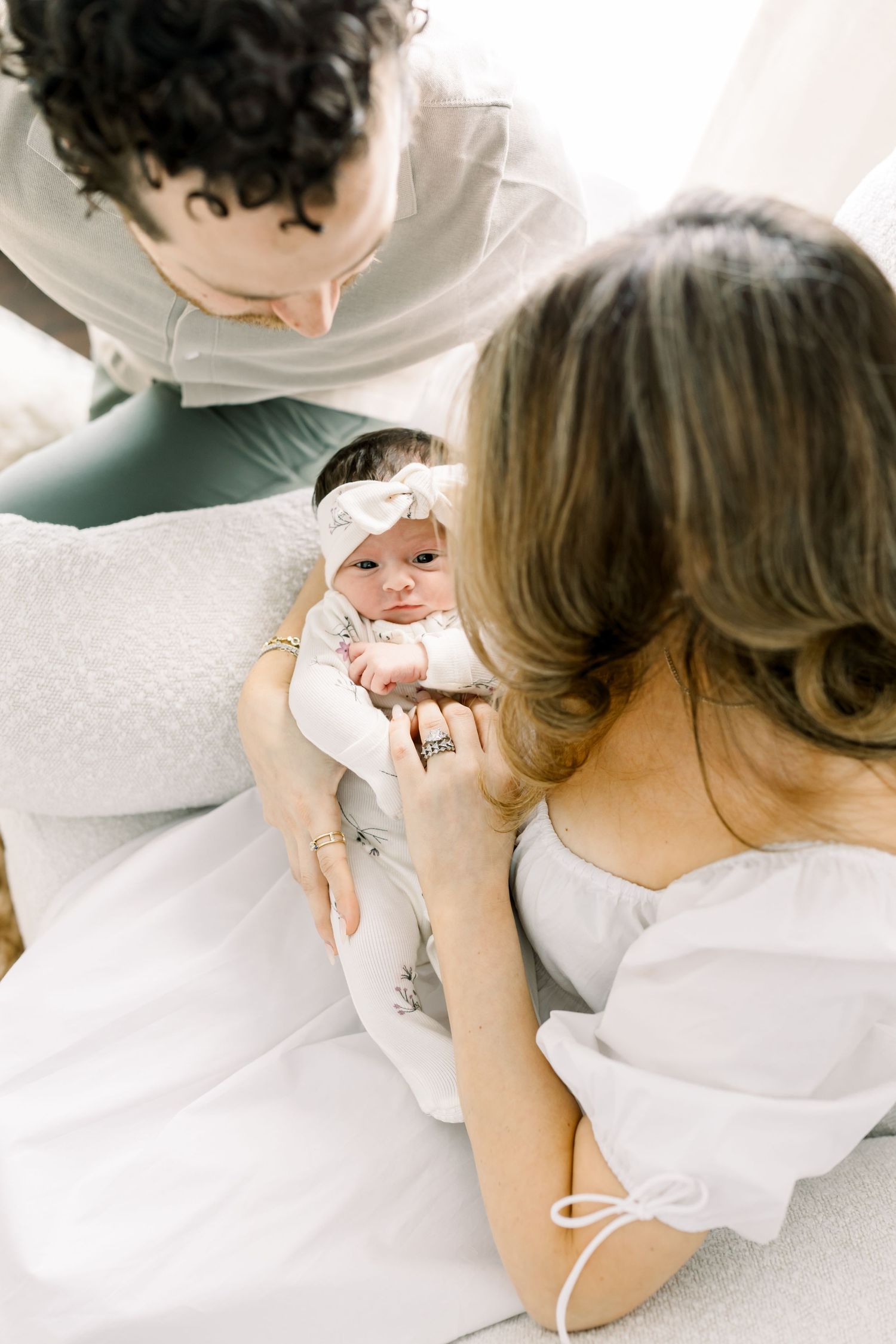 A sweet moment with a baby wearing a white headband and floral outfit on white bedding.