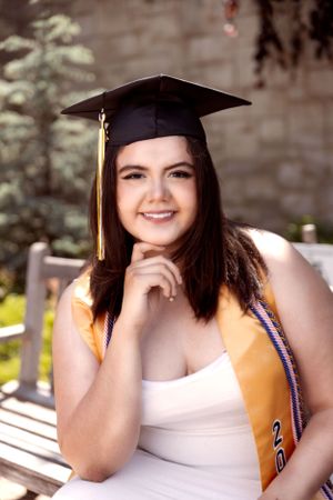 Graduate in yellow stole and cap poses outdoors for celebratory portraits.