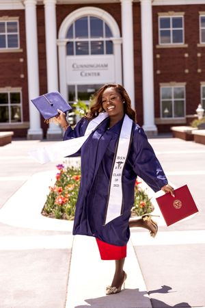 Graduate in purple cap and gown celebrates on campus steps with joyful poses and a diploma in hand.