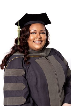 Graduate in black cap and gown with dark curly hair smiles during graduation photo session.