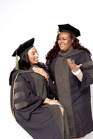 Two graduates in black academic regalia and mortarboards share a joyful moment during graduation.