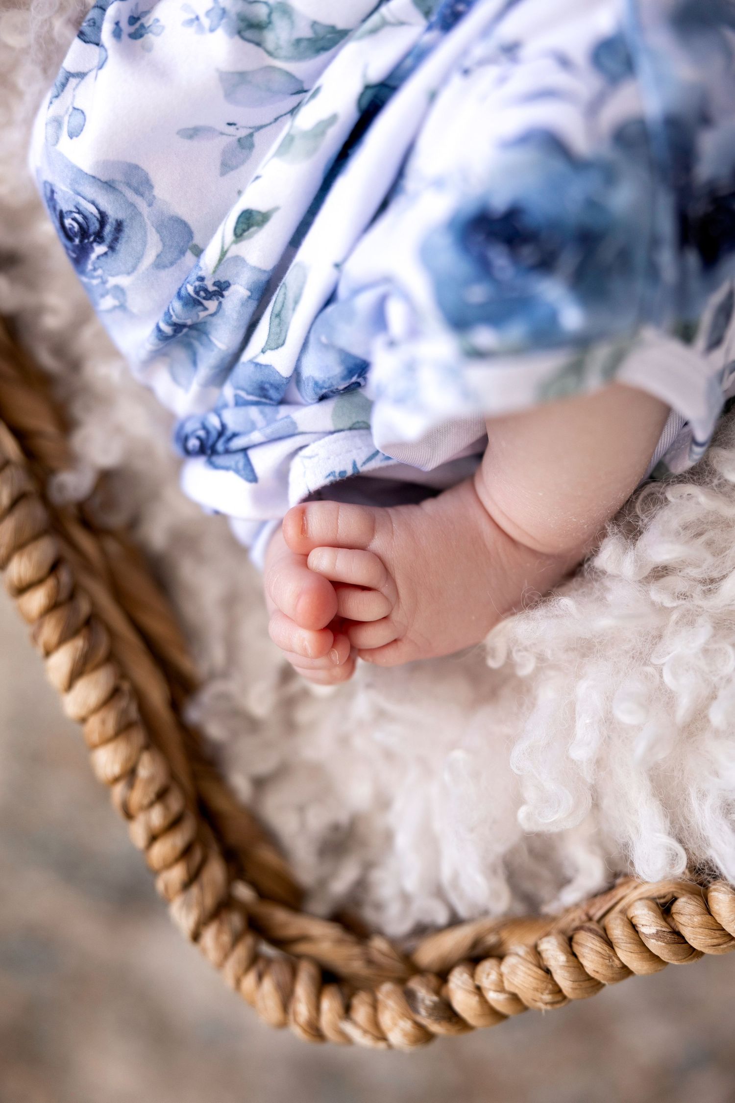 Close-up of tiny baby feet in blue patterned clothing on textured rope basket.