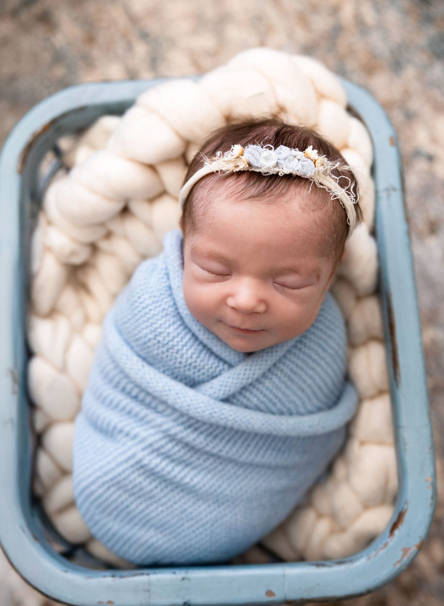 Newborn wrapped in blue swaddle sleeping peacefully in vintage blue container.