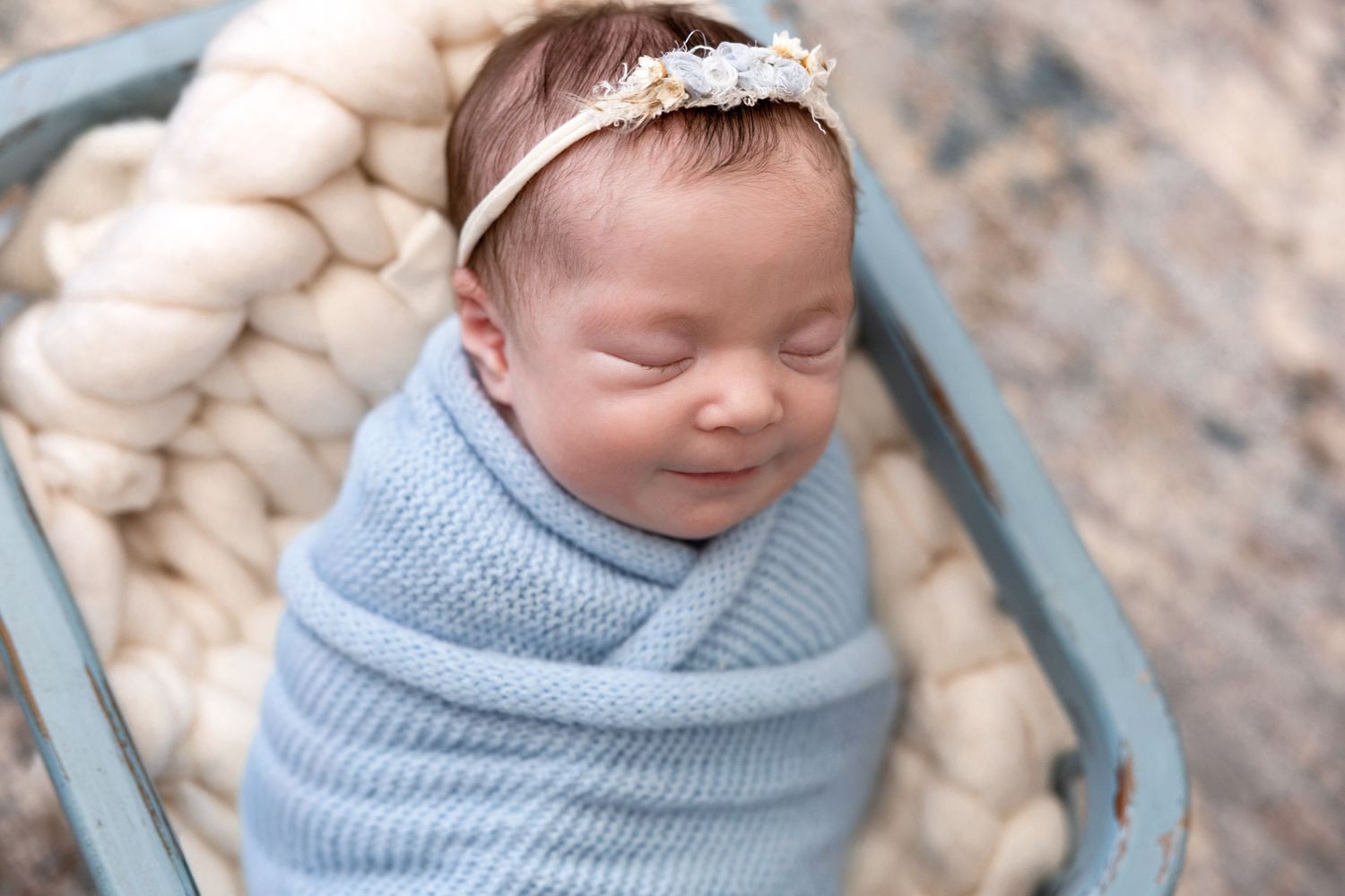 Sleeping newborn in blue wrap and headband photographed from above.